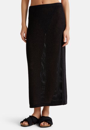 Gonna maxi nera in maglia con vestibilità ampia, caratterizzata da un motivo a rete testurizzato e una vita alta. Abbinata a sandali neri con zeppa.