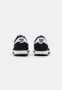 Mustat ja valkoiset Nike-kengät, joissa on mokka- ja verkkomateriaaleja, varustettuna 'Nike Air' -logolla kantapäässä, pehmustetulla varrella ja kumipohjalla.