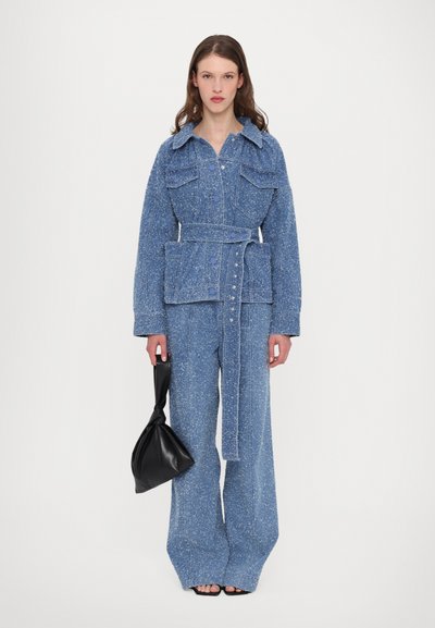 Set de jachetă și pantaloni din denim de culoare albastră deschisă, cu un finisaj texturat, având talie cu curea, buzunare tip patch și închidere cu nasturi. Geantă de mână neagră.