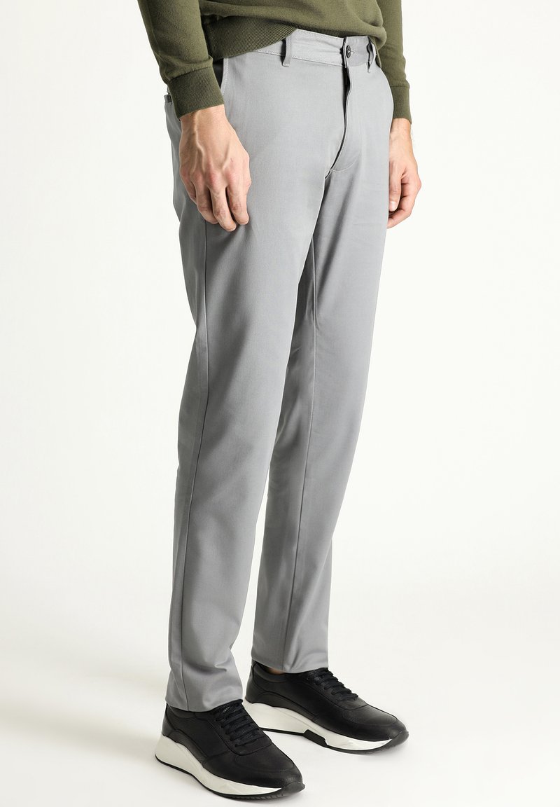 Pantaloni grigi realizzati in un tessuto liscio, con un design slim, tasche frontali e vita piatta. Abbinati a sneakers nere per un contrasto.