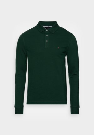 Polo à manches longues vert foncé avec trois boutons et un petit logo rouge, blanc et bleu sur le côté gauche de la poitrine.