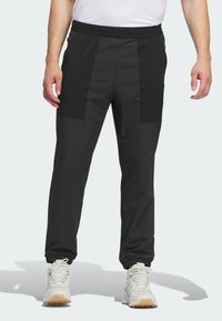 Juodos sportinės kelnės su tekstūruotu paviršiumi, pasižyminčios kontrastingais matiniais audinio intarpais, elastingu juosmeniu ir elastinėmis apyrankėmis ties kulkšniais.