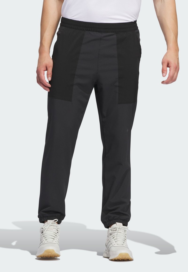 Juodos sportinės kelnės su tekstūruotu paviršiumi, pasižyminčios kontrastingais matiniais audinio intarpais, elastingu juosmeniu ir elastinėmis apyrankėmis ties kulkšniais.