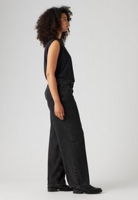 Zwarte top met mockneck, gecombineerd met hoge, losse zwarte denim jeans. Beschikt over strakke lijnen en een minimalistisch ontwerp. Zwarte enkellaarsjes maken de look compleet.