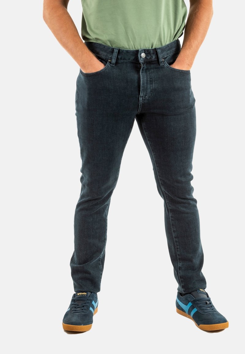Jeans in denim blu scuro con una vestibilità slim, cinque tasche e cuciture a contrasto, abbinati a sneakers blu scuro con strisce azzurro chiaro.