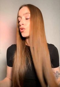 Giovane con capelli lunghi e lisci che indossa una maglietta nera, guarda di lato, con un piccolo tatuaggio visibile sul braccio sinistro.