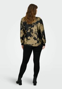 Blusa con motivo nero e oro, con finitura testurizzata, caratterizzata da maniche lunghe e una vestibilità rilassata, abbinata a jeans skinny neri e stivali con tacco.