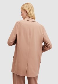 Világos rózsaszín blazer laza szabással, nyakkivágással, egy hátsó hasítékkal és két oldalsó zsebbel, sima, szőtt anyagból készült.