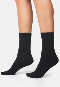 Sorte bomuldsstrømper med ribbet top, kort længde og glat tekstur. Strømperne har minimal branding på sålen.