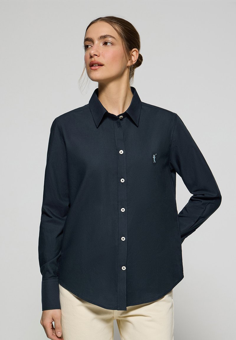 Camicia blu naval con bottoni, realizzata in tessuto liscio; presenta un colletto classico, maniche lunghe e una piccola figura ricamata sul petto.