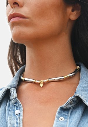 Collier ras-du-cou en ton argent et or avec des perles métalliques allongées et lisses ainsi qu'un pendentif décoratif en forme de feuille. Accents texturés.