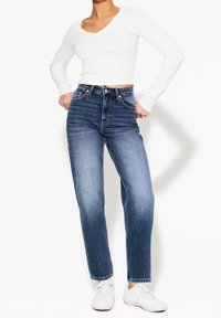 Džíny s vysokým pasem v tmavě modré barvě se mírně zúženou nohavicí, obsahující pět kapes a knoflíkový zip. Kombinované s bílým topem s dlouhým rukávem.