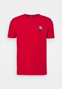 Červené bavlněné tričko s malou černobílou karikaturní postavičkou se slunečními brýlemi na levé části hrudi. Kulatý výstřih a krátké rukávy.