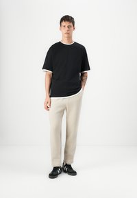 Black short-sleeve shirt with white trim, beige sweatpants, and black sneakers. Simple design, casual fit, and soft texture.