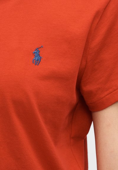 Piros rövid ujjú pamut póló, bal mellrészen kék hímzett póló játékos logóval. Simaságú anyag.