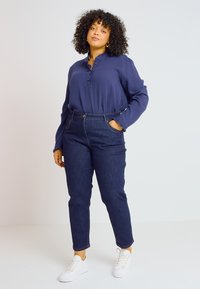 Blusa de botones azul marino con tejido texturizado, combinada con pantalones de mezclilla oscuros de tiro alto y zapatillas blancas, con un ajuste relajado.