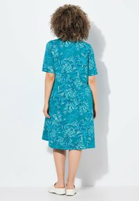 Vestido de manga corta en color verde azulado con un patrón de hojas, que presenta un ajuste holgado y una longitud hasta la rodilla. La tela tiene una textura suave.