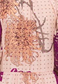 Kukallinen mekko, jossa on pehmeän vaaleanpunainen tausta. Mekossa on oransseja ja purppuranvärisiä kukkia, pilkkuja ja kerätty vyötäröyksityiskohta.