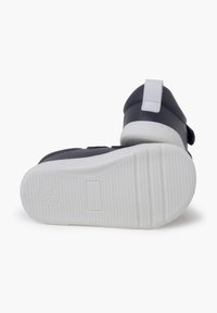 Black and white children's shoes with a textured white rubber sole, adjustable strap, and navy upper, featuring a reinforced heel and toe.