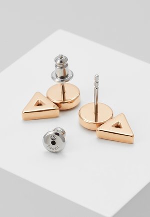 Paire de boucles d'oreilles clous triangulaires en or rose avec attaches papillon argentées présentées sur une surface blanche.