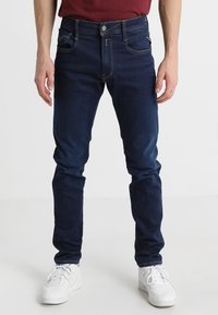 Mörkblå denimjeans med en smal passform, utrustade med två framfickor och en liten myntficka, avslutade med en metallknapp och dragkedjegylf.