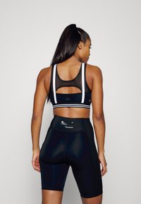 Top desportivo preto em tecido de rede com riscas brancas, combinado com calções pretos de cintura alta que apresentam um detalhe de logótipo na cintura.