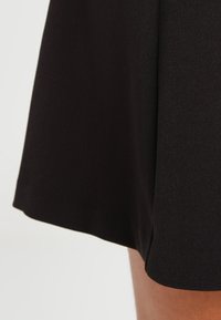 Falda negra con un acabado suave y texturizado. Dobladillo ligeramente acampanado y detalle de costura limpio. La tela parece duradera y ligera.