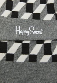 Sive čarape s geometrijskim crno-bijelim uzorkom; sadrži logo "Happy Socks" u bijeloj boji na strukturiranoj pozadini.