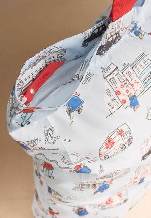 Geantă de pânză cu ilustrații tematice din Londra, inclusiv clădiri, vehicule, oameni și o mâner roșu, prezentând un buzunar cu fermoar deschis.