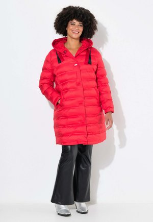Red puffer coat with hood, featuring horizontal stitching, pocket detail, and black straps on shoulders. Worn with flared black pants and silver boots.