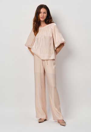 Lichtroze, vloeiende blouse met pofmouwen en een geraffineerde halslijn, gecombineerd met bijpassende losvallende broek; gladde, lichte stof en gestructureerde schoenen.