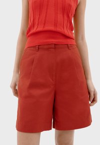 Shorts en coton rouge avec un design ajusté, devant plissé et poches latérales. Longueur mi-cuisse avec une texture lisse et une finition soignée.