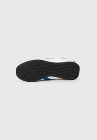 Talpa de pantof cu un fund din cauciuc texturat, de culoare neagră, având un model în fagure și un design superior de culoare deschisă, cu accente albastre.