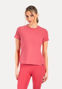 Camiseta deportiva de manga corta rosa con cuello redondo, hecha de tela lisa, combinada con leggings a juego.