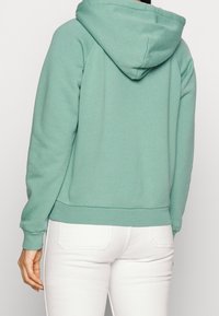 Sudadera verde menta con bolsillo canguro, puños y dobladillo acanalados, y capucha con cordón. Tejido suave con una textura lisa, ajuste casual.