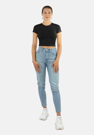 Schwarzes kurzer Pullover, kombiniert mit hellblauen high-waist Jeans und weißen Sneakers. Einfaches Design, taillierte Form, glatte Stofftextur.