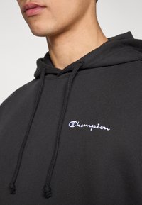 Μαύρο φούτερ με κουκούλα από βαμβακερό μείγμα ύφανσης. Διαθέτει τσέπη στο μπροστινό μέρος, κορδόνια και λευκό κεντημένο λογότυπο "Champion".