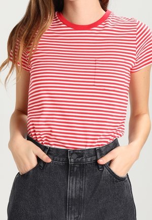 Femme portant un t-shirt à manches courtes rayé rouge et blanc rentré dans un jean noir taille haute, les mains dans les poches.