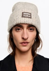 Jasnoszara, dziergana czapka beanie o miękkiej fakturze, z tkanym metkiem z napisem "BIMBA YLOLA." Zawiera subtelne srebrne akcenty.