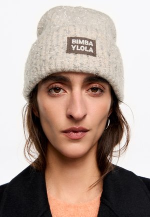 Gorro tejido de color gris claro con una textura suave, que presenta una etiqueta tejida que dice "BIMBA Y LOLO." Incluye sutiles acentos plateados.