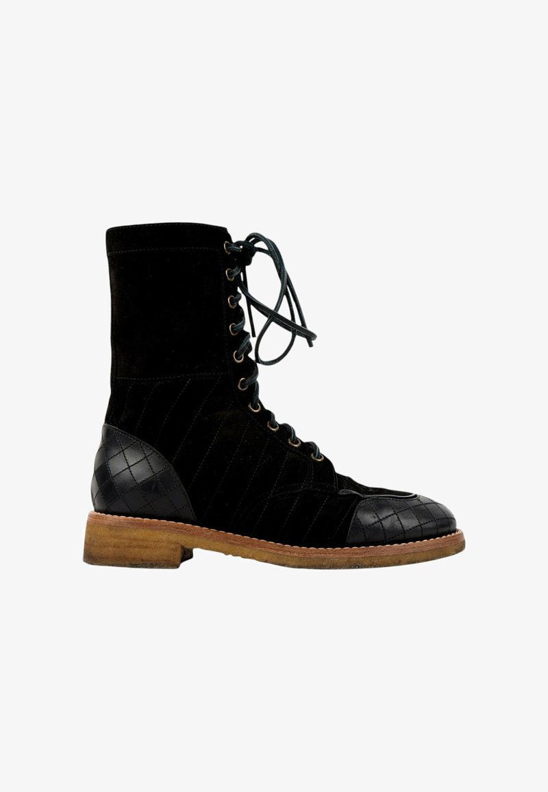 Bottine noire à lacets avec panneaux matelassés sur le bout et le talon, et une semelle en bois marron, présentée sur fond blanc.