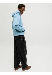 Sudadera azul clara con un bolsillo frontal, combinada con pantalones de pierna ancha negros que tienen un bolsillo trasero. Unos zapatos marrones con cordones completan el conjunto.