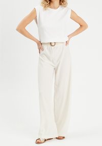 Crop-top in white fabric with cap sleeves paired with loose, light beige trousers featuring a textured weave and a braided belt.