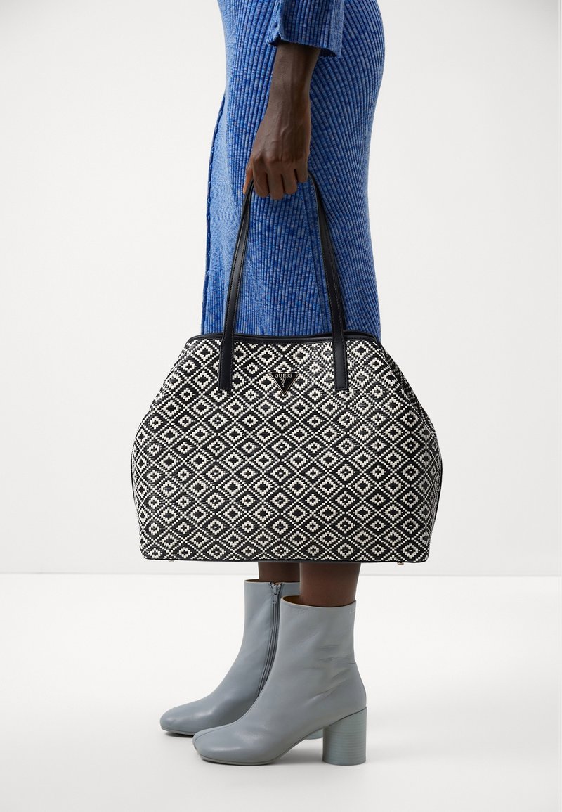 Černobílá taška s vzorem a diamantovým designem, s černými ušima a kovovým logem na přední straně.