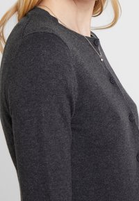 Grafitowy szary kardigan wykonany z miękkiego materiału, z okrągłym dekoltem, długimi rękawami oraz czarnym zapięciem na guziki z przodu.