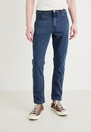 Blugi din denim de culoare albastră închisă, cu un design slim fit, având un stil clasic cu cinci buzunare, bucle pentru curea și închidere cu fermoar.