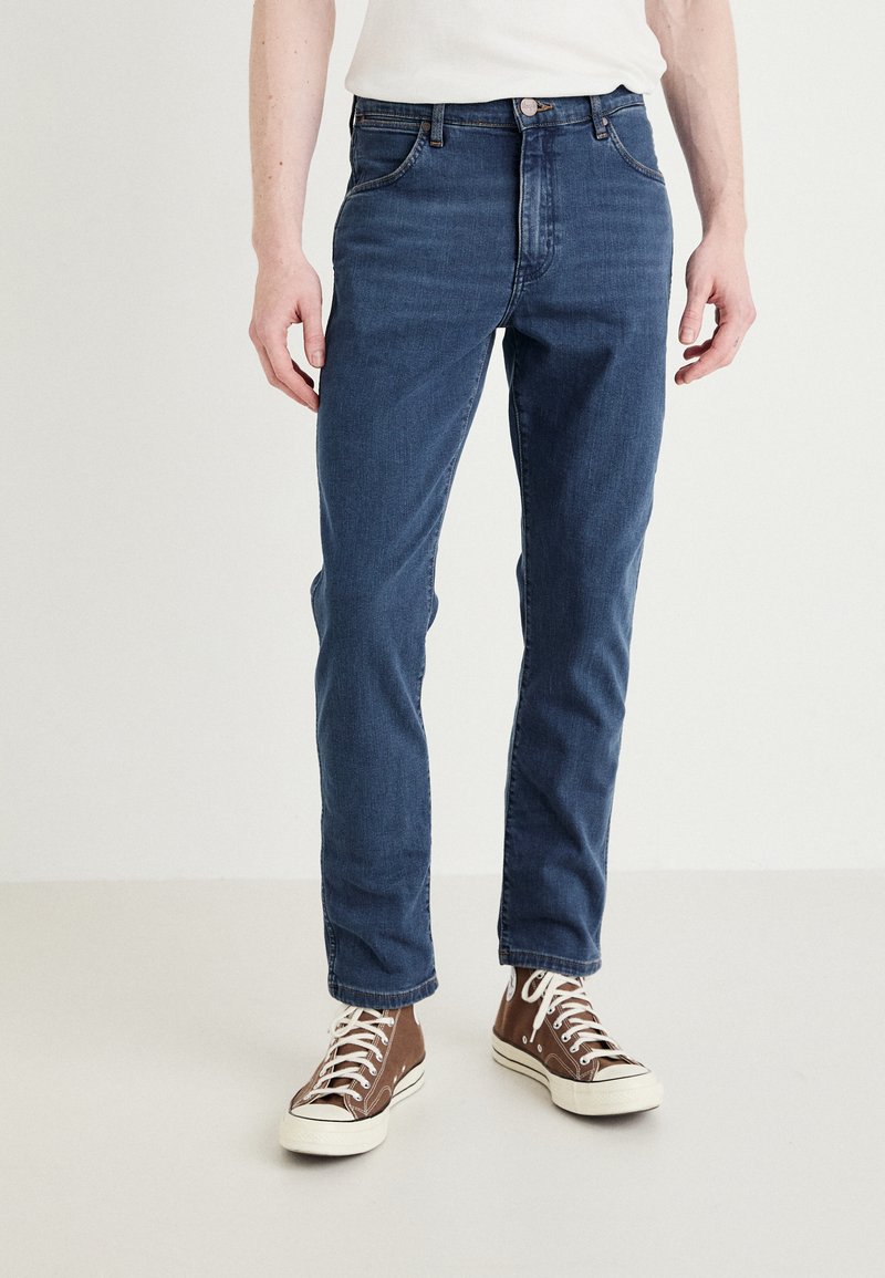 Τζιν παντελόνι σε σκούρο μπλε χρώμα με στενή γραμμή, διαθέτοντας κλασικό στιλ πέντε τσεπών, θηλιές ζώνης και κλείσιμο με φερμουάρ.