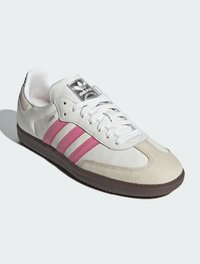 Sneaker bianco in pelle con strisce rosa, texture liscia, punta rotonda e suola in gomma marrone. Presenta un logo argentato sulla linguetta.