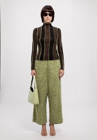 Un col roulé rayé marron, un pantalon large en peluche vert, des lunettes de soleil noires et un sac à main vert clair à la texture lisse.