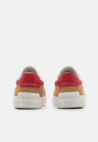 Paire de baskets basses en daim beige, avec des languettes rouges au talon portant la mention "Depuis 1973", et des semelles en caoutchouc blanc estampillées "Pepe Jeans London".